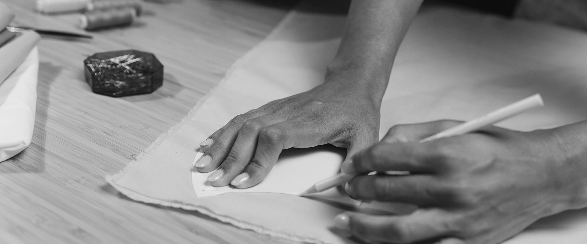 Hands marking and cutting a pattern on the atelier table